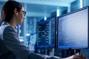 Close-up Shot of Female IT Engineer Working in Monitoring Room. She Works with Multiple Displays.